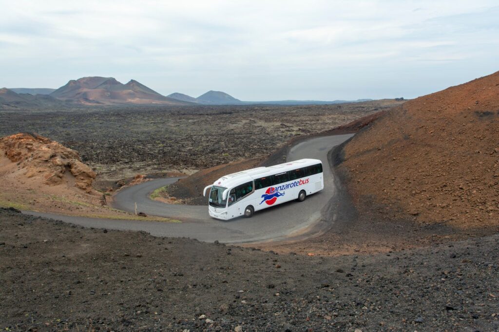 A coach bus winding through the volcanic terrain of Lanzarote, Spain, showcasing the island's unique arid beauty.