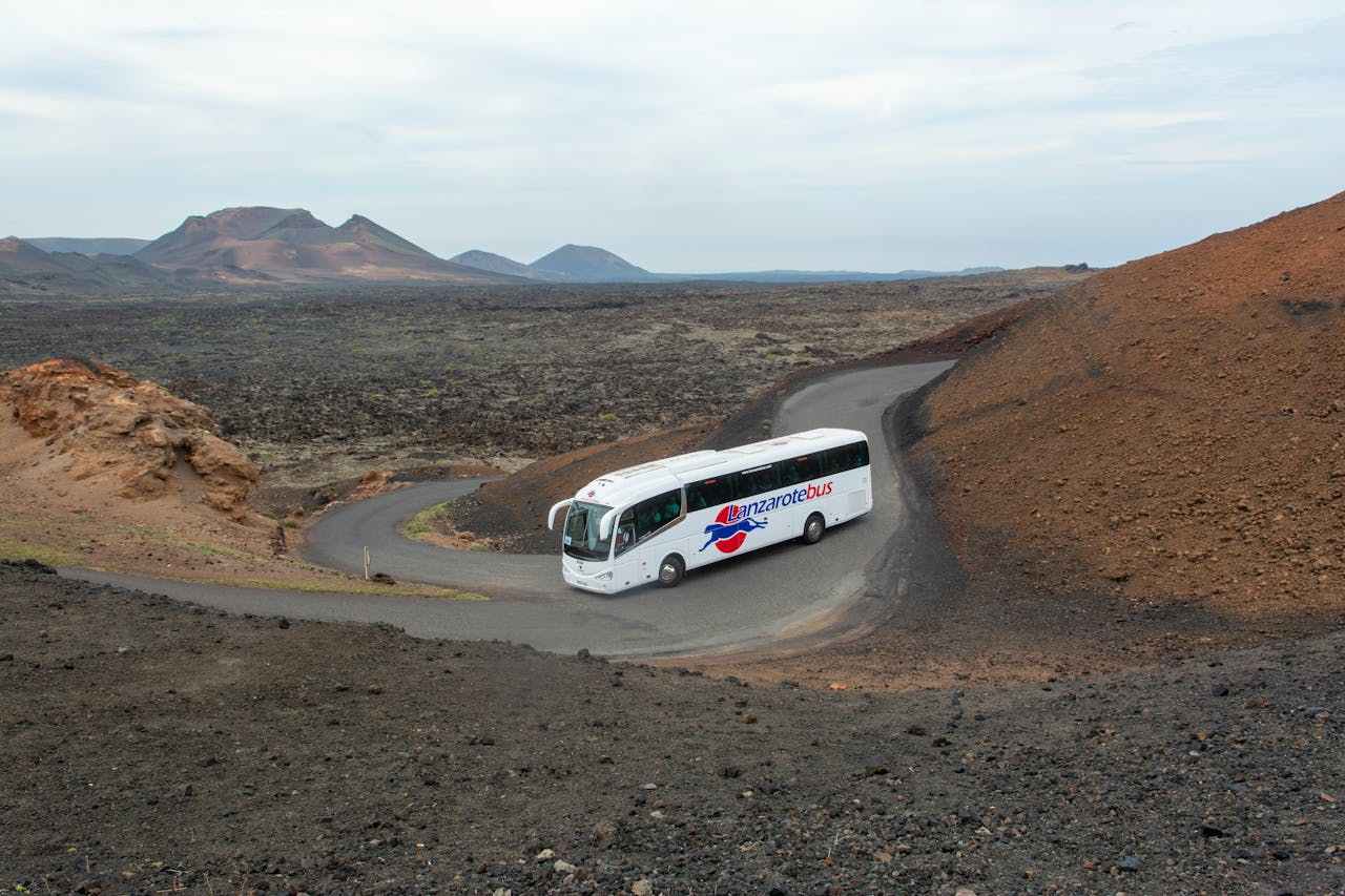 A coach bus winding through the volcanic terrain of Lanzarote, Spain, showcasing the island's unique arid beauty.